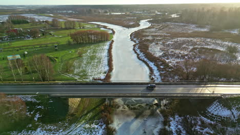 coche conduciendo a través del puente sobre el río congelado en invierno