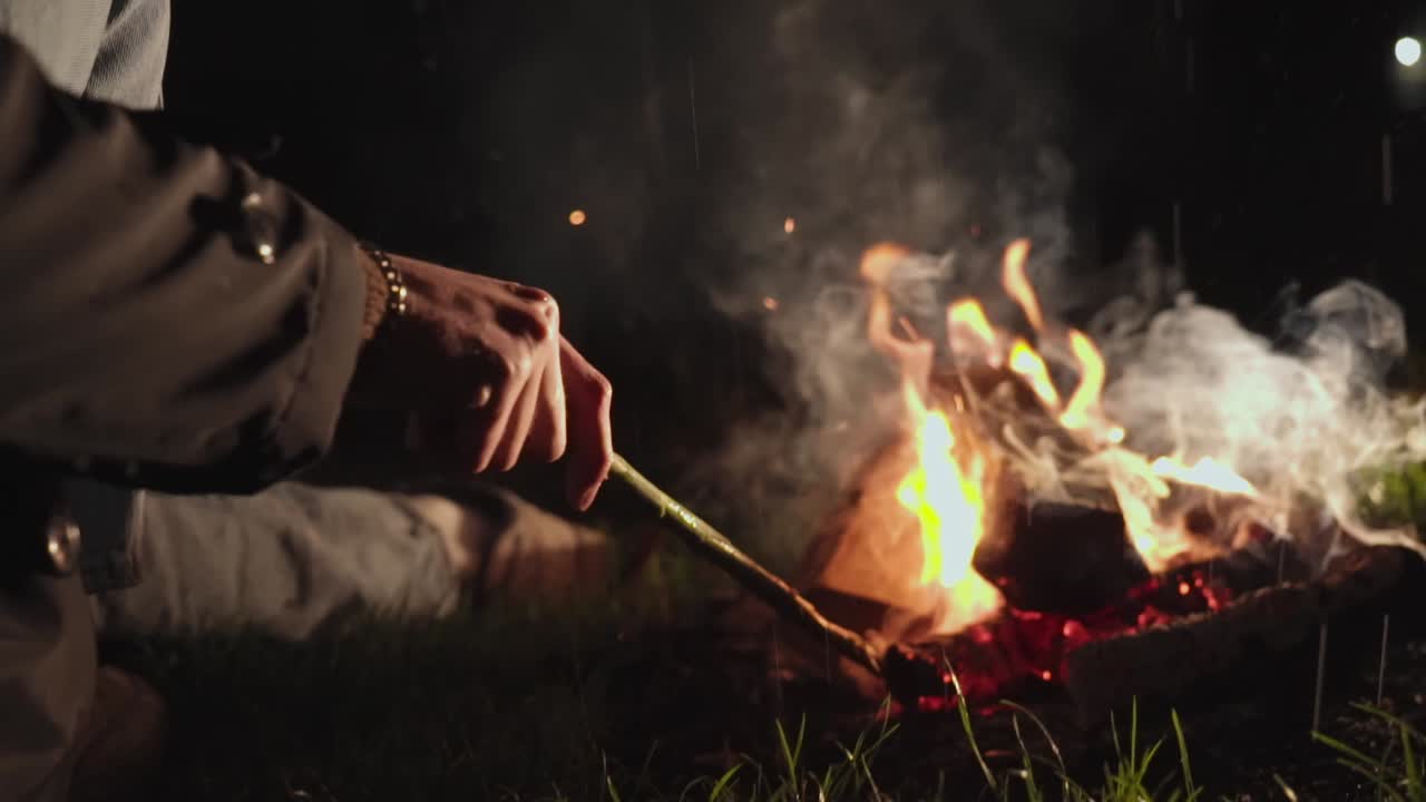 Person Sitting by a Campfire at Night in the Rain
