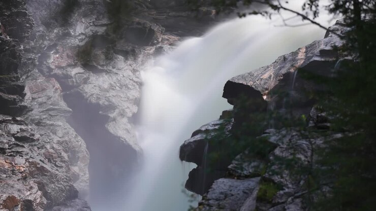 Una cascata potente e tumultuosa scende a cascata sulle pietre scure in mezzo alla foresta estiva