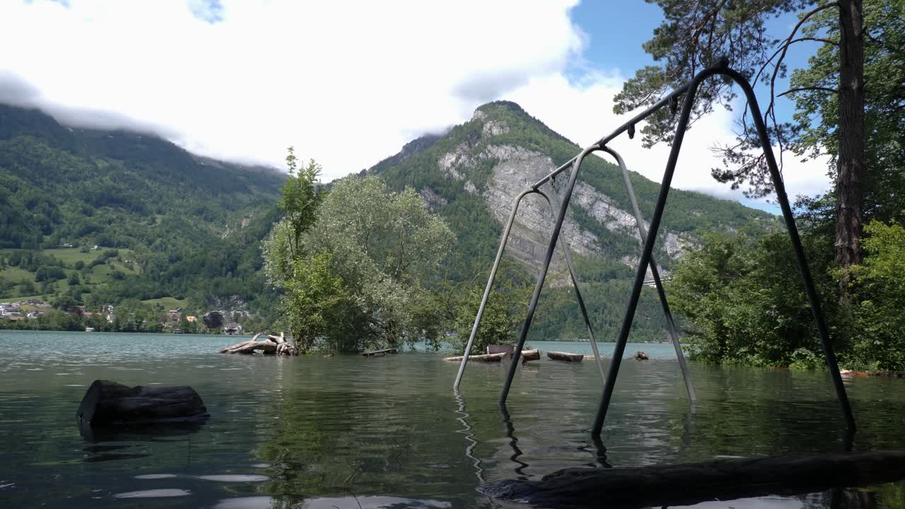 el parque infantil con un columpio en suiza está inundado y abandonado frente a una gran montaña en un día soleado