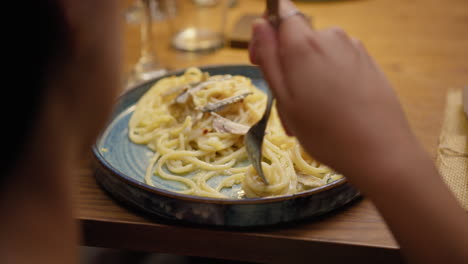 woman rotating the fork to grab spaghetti with anchovies during a dinner