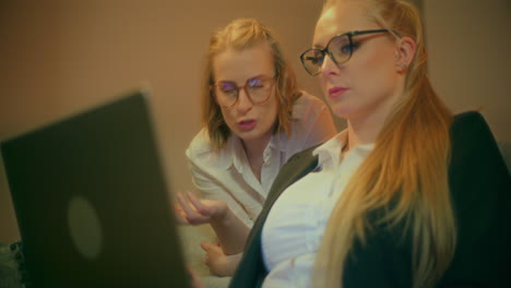 two female coworkers discuss project on laptop during evening meeting