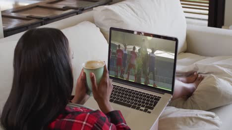 compuesto de una mujer sentada en casa sosteniendo un café viendo un partido de hockey en una computadora portátil