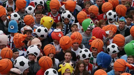 a colorful crowd of fans wearing unique sport-themed hats at a vibrant event, showcasing a blend of basketball and soccer enthusiasm among cheerful spectators