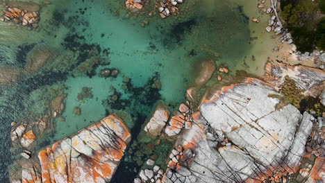 aerial of bay of fires bright orange rocks with waves in rock pools in the sea