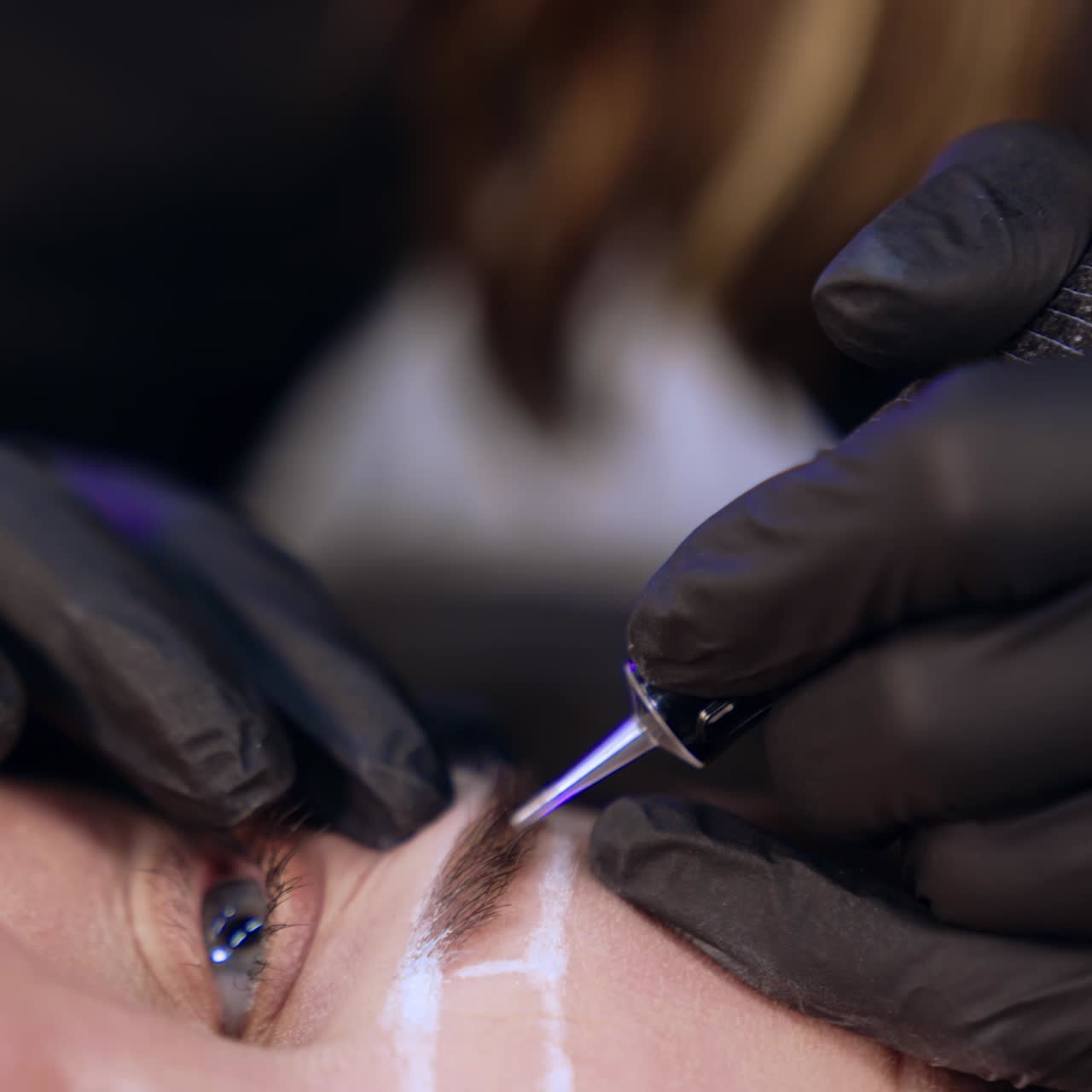 Special tool for permanent make up in the gloved hands of beautician. Eyebrow procedure for a female client at salon. Close up