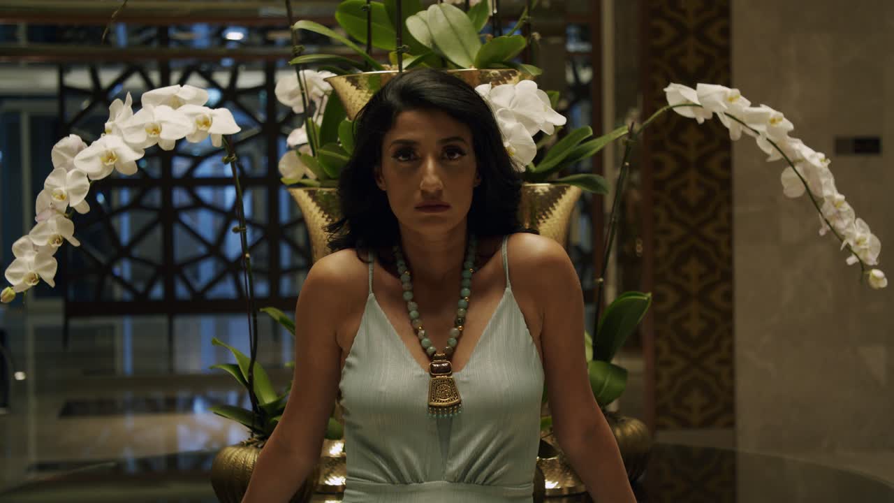 우아한 여성은 오버헤드 조명과 꽃병을 배경으로 카메라를 바라보고 있습니다 - 정적, 중간 샷