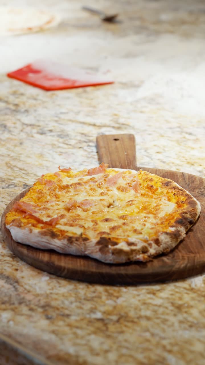 Slow vertical focus pull revealing a freshly baked ham pineapple and cheese Hawaiian pizza served on a wooden board at a kitchen table