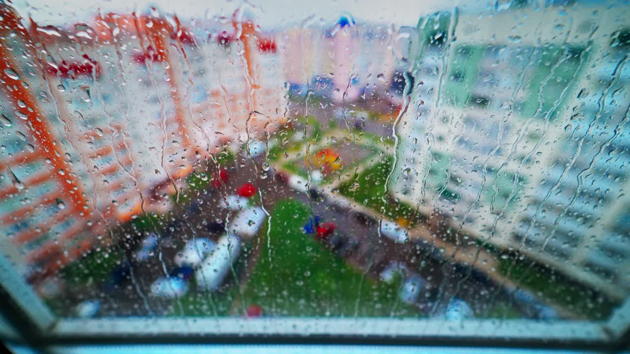 Water drops flowing down on glass on the city background. Rainy weather. Raindrops on glass window. Drops moving along glass.