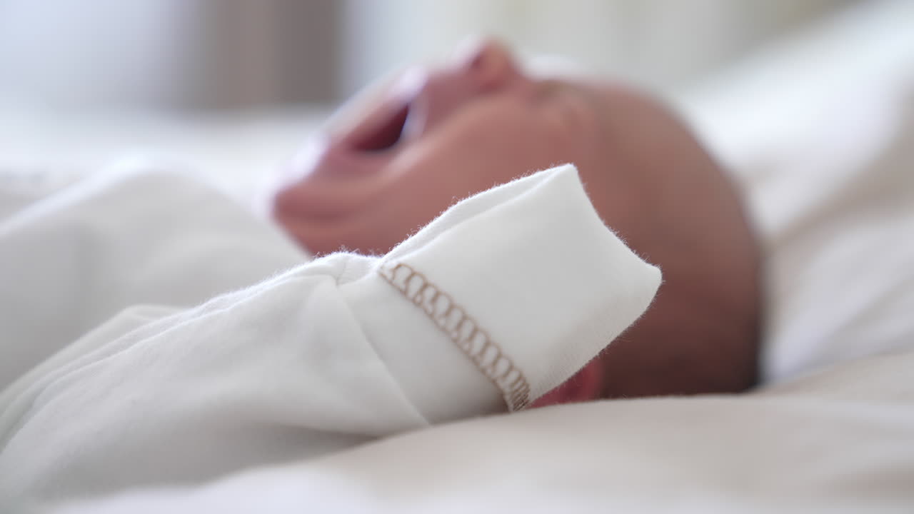 Neonato in una camicetta chiara si sveglia e fa smorfie. Primo piano di neonato in vestiti bianchi.