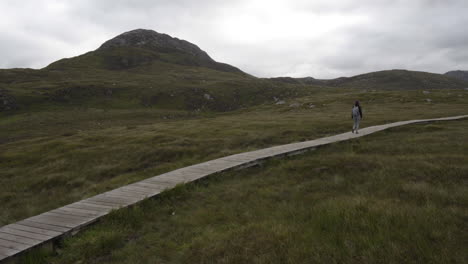 girl walking, hiking in connemara national park on a wooden planked trail with diamond hill in the background, ireland 4k