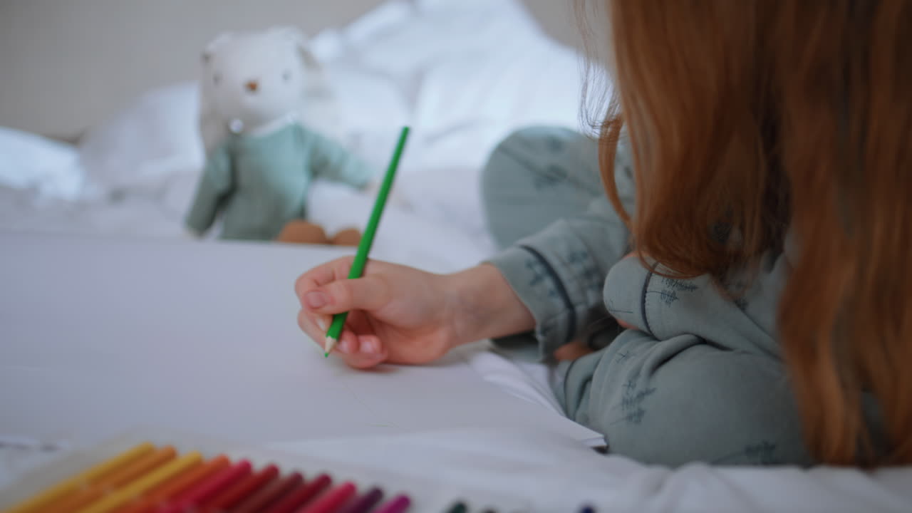 週末に子供が紙に鉛筆で描画しているクローズアップ。マットレスに座っている見知らぬ少女。
