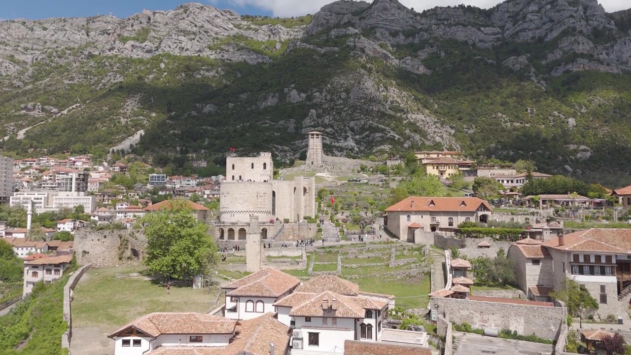 Ripresa aerea con tilt verso l'alto dalle case del centro storico di Krujë, che rivela le maestose montagne sullo sfondo, Albania