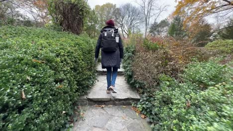 woman with a backpack walking along a stepped walkway in new york city's central park