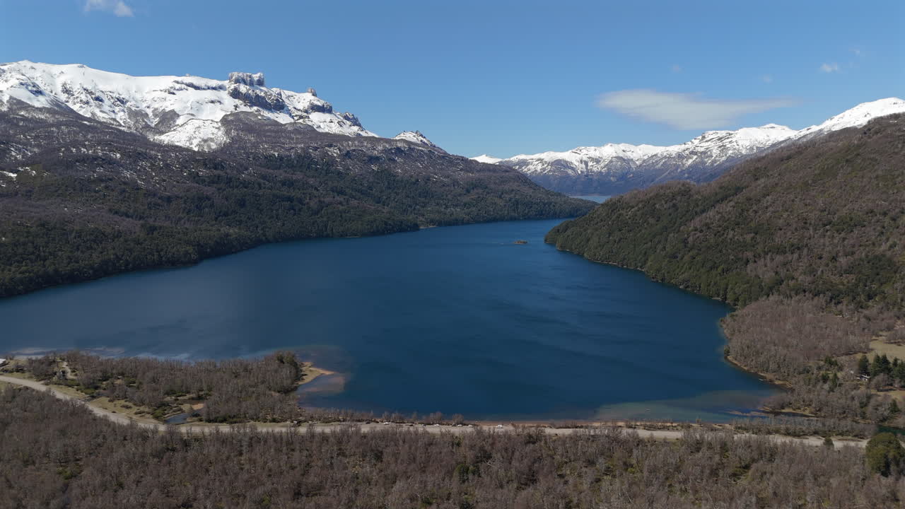 Aerial view of Lake Falkner in Argentina, surrounded by lush forests and framed by snow-capped Andean peaks.