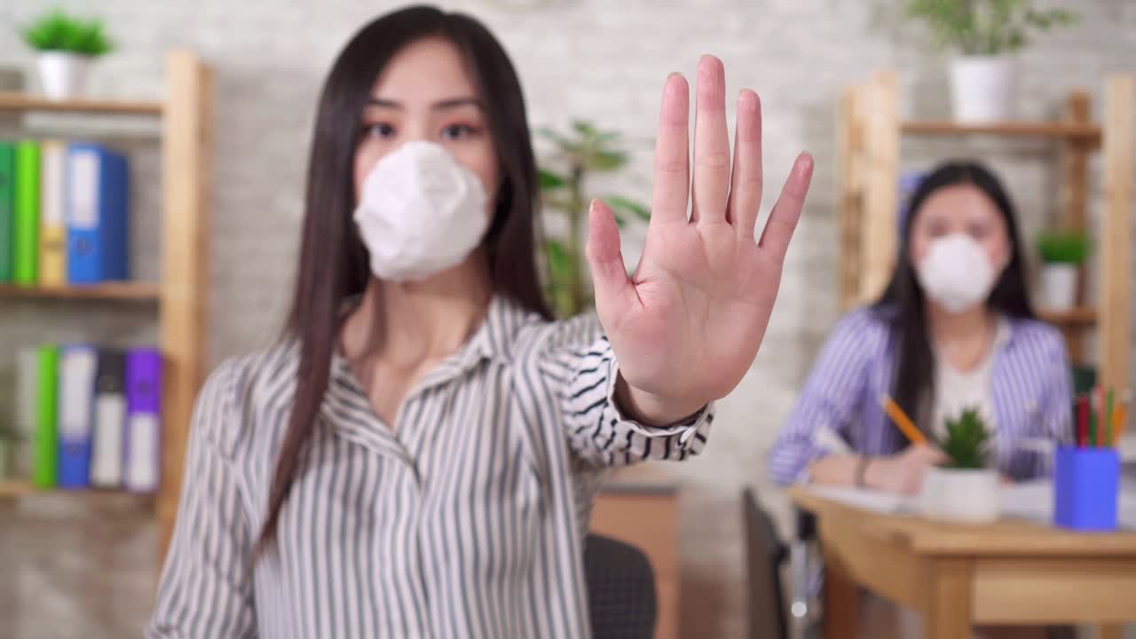 의료 보호 마스크를 입은 젊은 아시아 사무실 직원이 손을 고 멈추는 몸짓을 합니다.