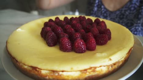 mira de cerca un pastel decorado con frambuesas. la mujer está adorando y decorando la parte superior del pastel con frambuesas en el