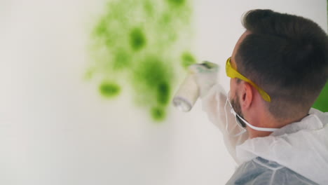 hombre con ropa de trabajo pinta la pared usando spray verde en la habitación