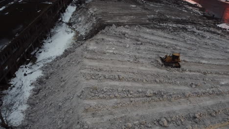 Bulldozer-pushing-sand-and-rocks,-evening-out-ground---aerial-view