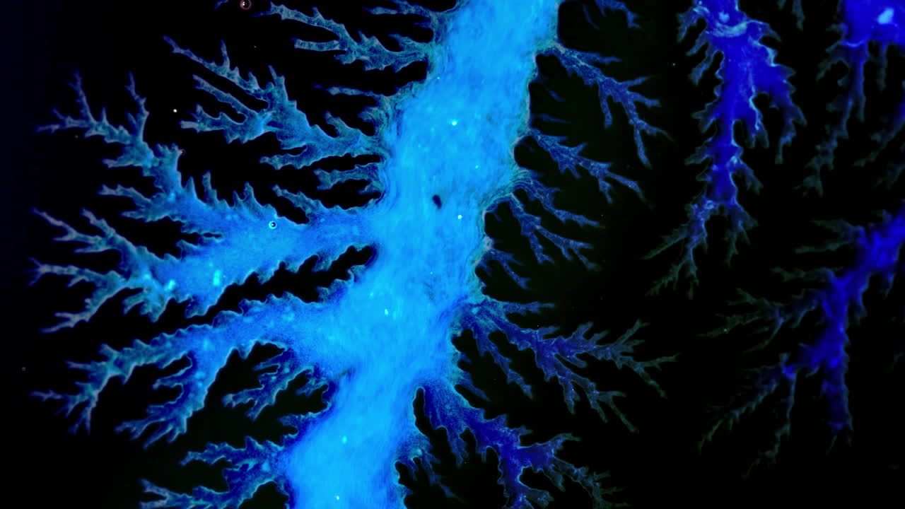 Blue ink spreading and branching on black surface in intricate patterns