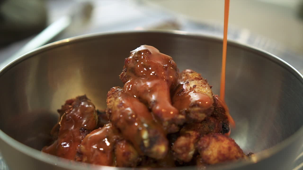 Pouring hot sauce on chargrilled chicken wings