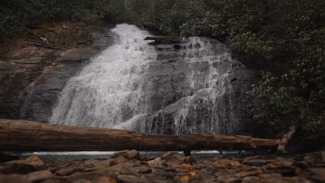 Pintoresca-Cascada-En-El-Bosque-Cayendo-En-Cascada-Por-La-Ladera-De-Una-Montaña-En-Cámara-Lenta-Con-Un-Tronco-En-Primer-Plano---Vista-Deslizante