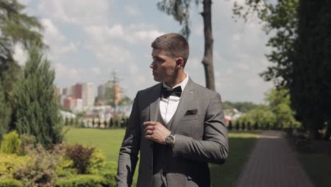 Groom-goes-down-the-alley-between-bushes-with-a-wedding-bouquet-to-his-beloved-bride,-first-meeting