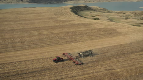 farm tractor seeding slowly moving on fields near serene lake in saskatchewan, canada