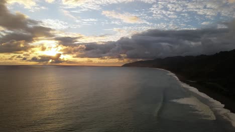 slow aerial shot flying over the ocean with cloudy sunset in the horizon