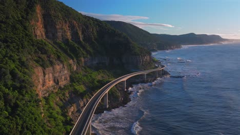 sunrise sea cliff bridge aerial drone view iconic famous stanwell park cars driving waves south coast nsw australia landscape royal national park wollongong coalcliff iiawarra sydney backwards pan up