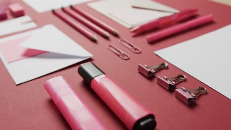 Close-up-of-pens,-pencils-and-stationery-arranged-on-red-background,-in-slow-motion