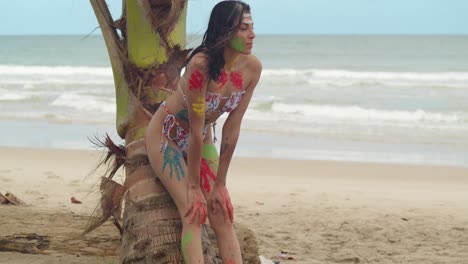 A-Caribbean-beach-is-the-backdrop-for-a-girl-in-body-paint-and-a-bikini-on-a-sunny-day-lean-on-a-coconut-tree