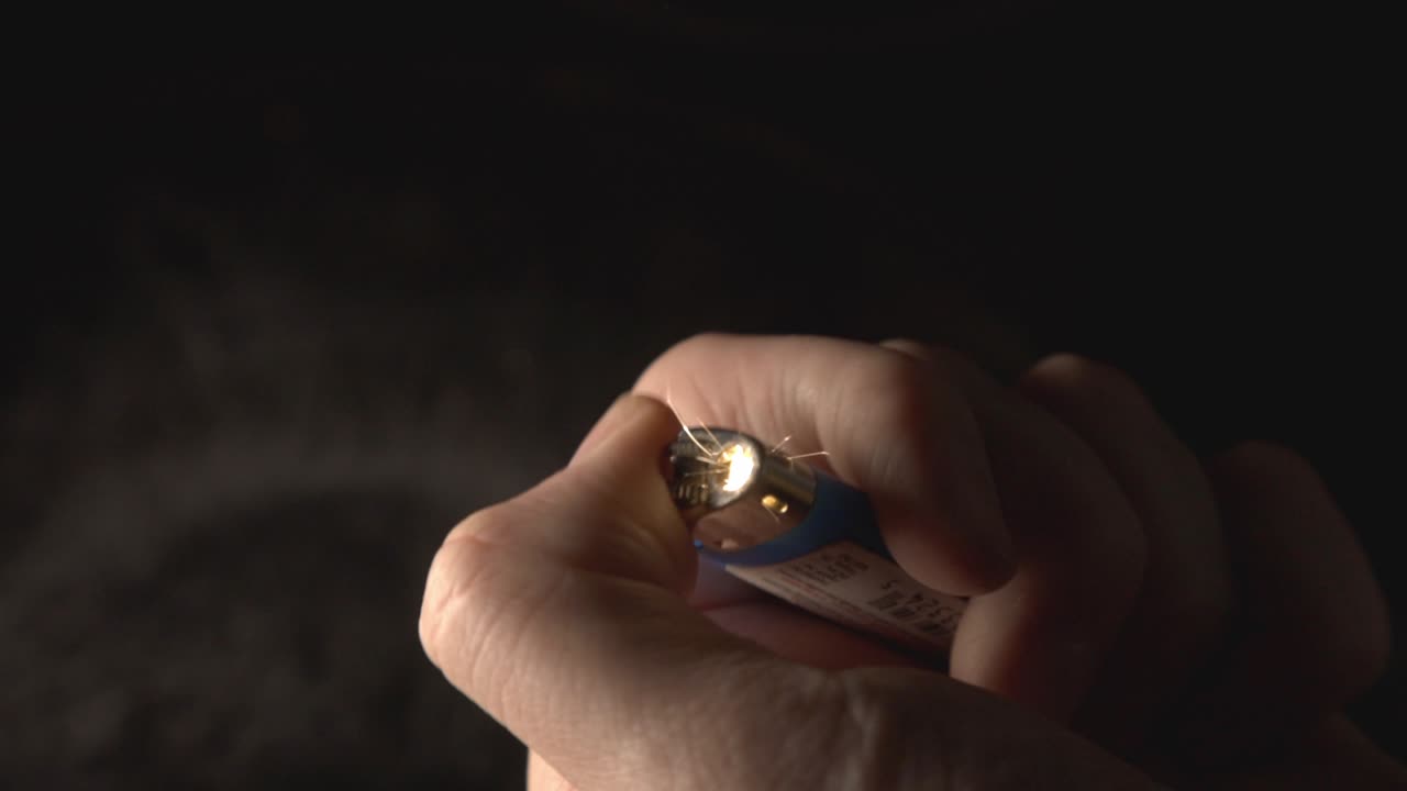 Primo piano di una mano che accende un accendino con luce sullo sfondo scuro.
