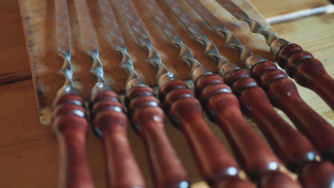 Close up of neatly aligned polished wooden skewers with glossy dark handles resting on rustic wooden table in cozy cabin interior with soft natural light creating warm inviting ambiance