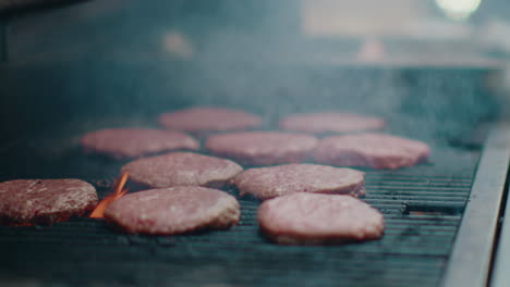 mouthwatering beef hamburgers smoking on an outdoor bbq grill, surrounded by smoke and flames dancing around the burgers.