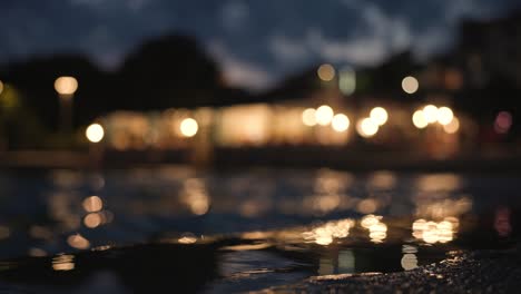 Low-angle-view-of-waves-on-sea-surface-at-coastline-after-sunset-with-night-club-in-the-background