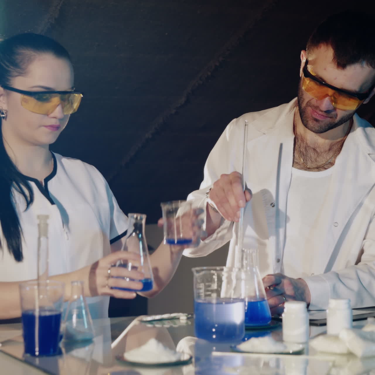 Two Technologists or scientist working in a chemical laboratory doing experiments with colorful solutions in beakers and test tube. Square video
