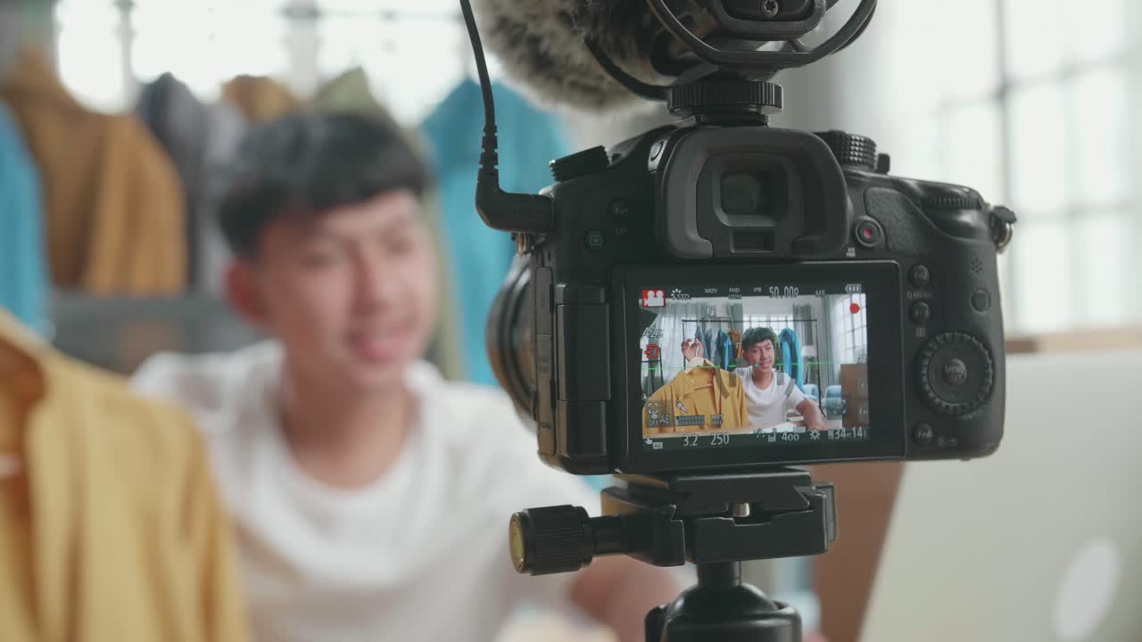close up de un monitor de cámara grabando a un joven asiático vendedor en línea recomendando una camisa mientras usa la computadora para vender ropa en casa