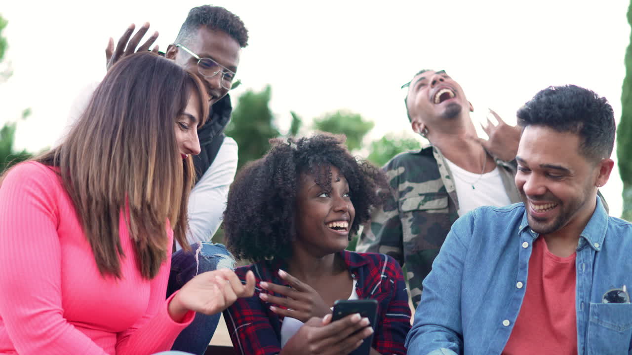 Diverse Group of Friends Laughing and Engaging with a Smartphone Outdoors