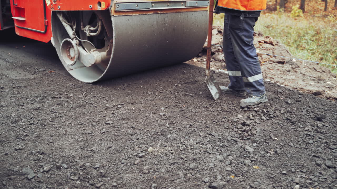 Workers in special uniform working with shovels making a new road. Compactor machine and workers putting new asphalt. Close-up