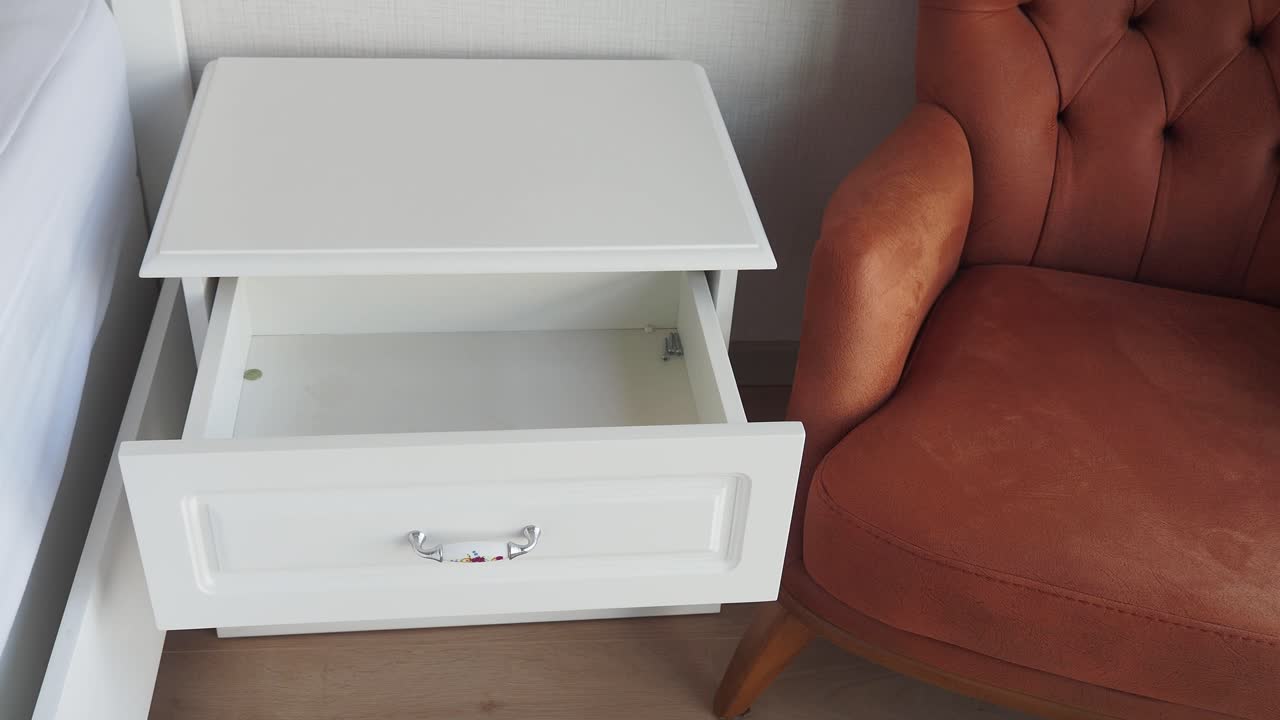 mesita de noche blanca con cajón vacío y silla marrón