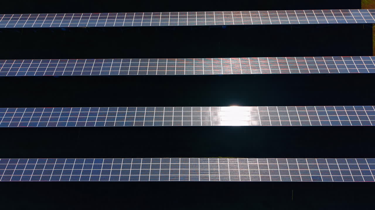 Luce solare che si riflette sulla superficie di pannelli solari fotovoltaici blu. Inquadratura dall'alto di pannelli solari con un intenso bagliore bianco del sole sulla superficie di vetro contro ombre scure.