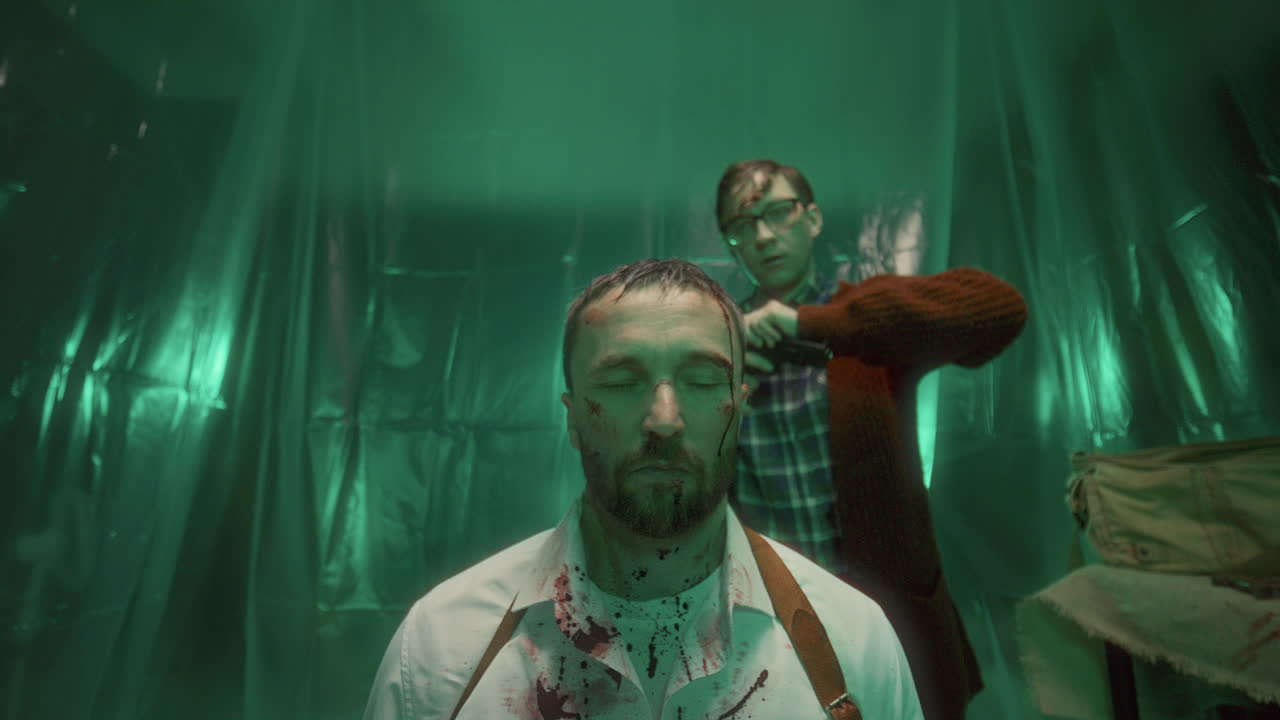 Maniac Walking to Trapped Man in Bloodstained Shirt, Threatening Him with Gun