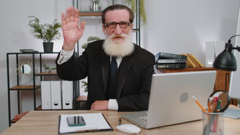 Businessman-working-on-laptop-smiling-friendly-at-camera-and-waving-hands-gesturing-hello-at-office