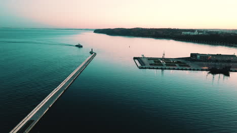 Drone-flying-around-military-ship-sailing-into-the-bay-at-the-sunset