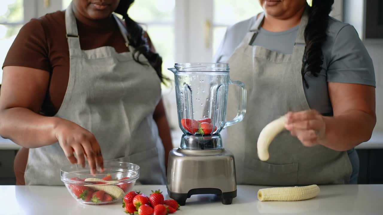 In cucina, due donne con grembiuli aggiungono fragole e banane al frullatore per un frullato.