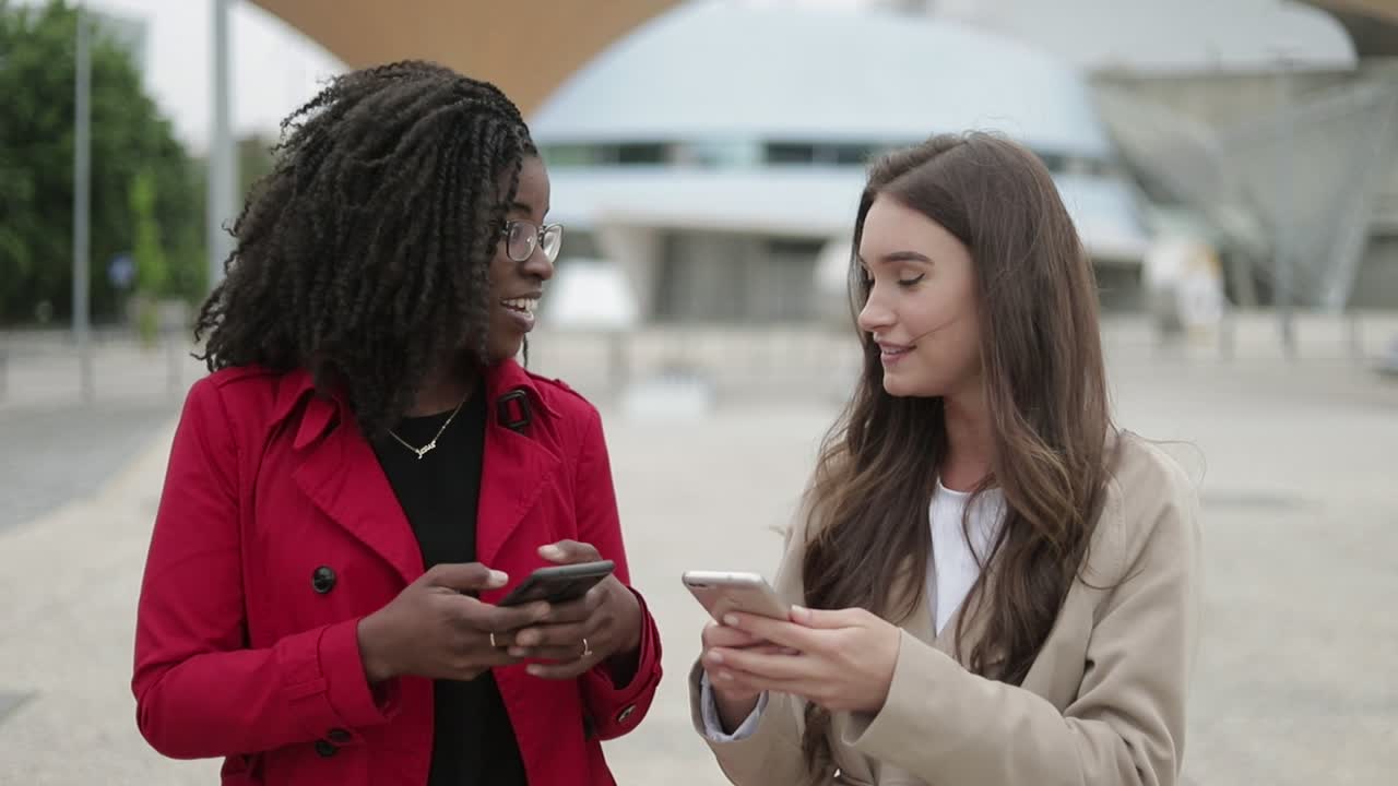 Two women walking along street, one showing pictures on phone