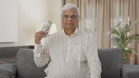 confident indian old man using money as fan