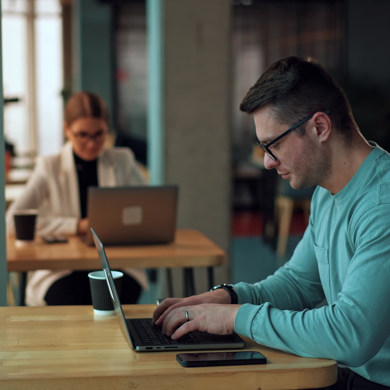 Office people working on laptops in the office. Focused man typing something on laptop. Woman works at backdrop