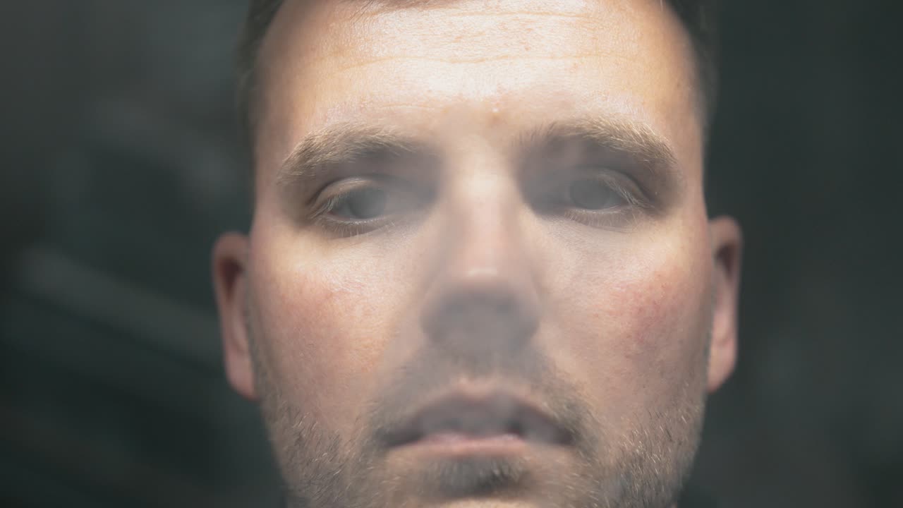 young man smokes vape and blows into the camera close up